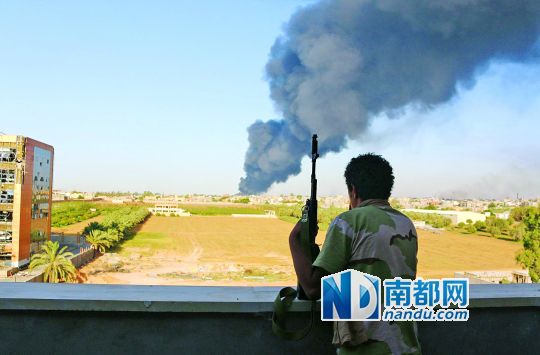 2日，利比亞首都的黎波里，一民兵武裝成員眺望被火箭彈擊中的儲油罐冒出濃煙。