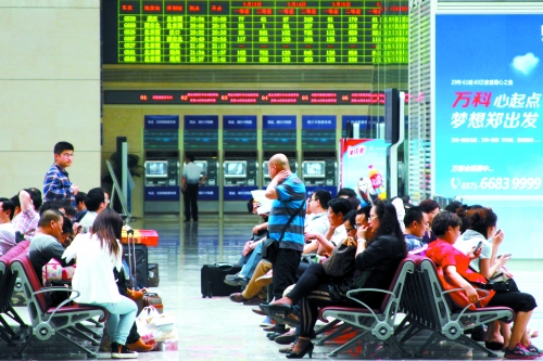 候車大廳溫度很高，一名乘客一手扇風(fēng)、一手擦汗