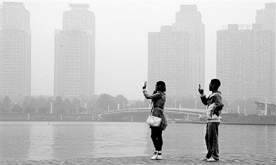 29日中午，鄭東新區(qū)如意湖畔，兩個(gè)年輕人拍攝霧霾中的景色。 鄭州晚報(bào)記者 馬健 圖