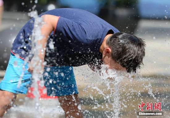 5月29日，一名小孩將頭伸向北京街頭的噴泉以降溫祛暑。