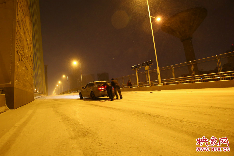 雪天路滑，汽車上橋打滑，兩名“推車人”幫助一輛私家車上坡。