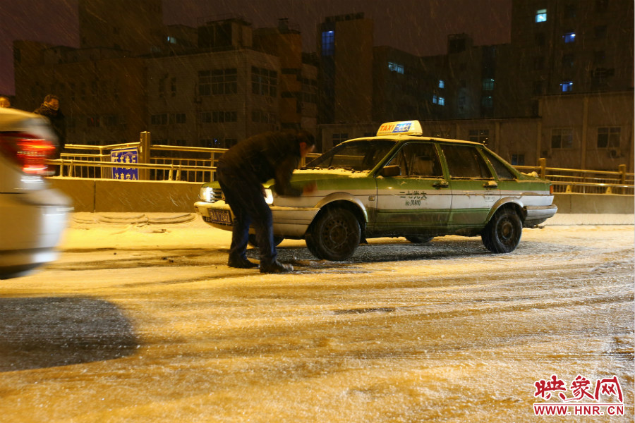 一位出租車司機在車輪前灑上雪，希望能增加輪胎的摩擦力。