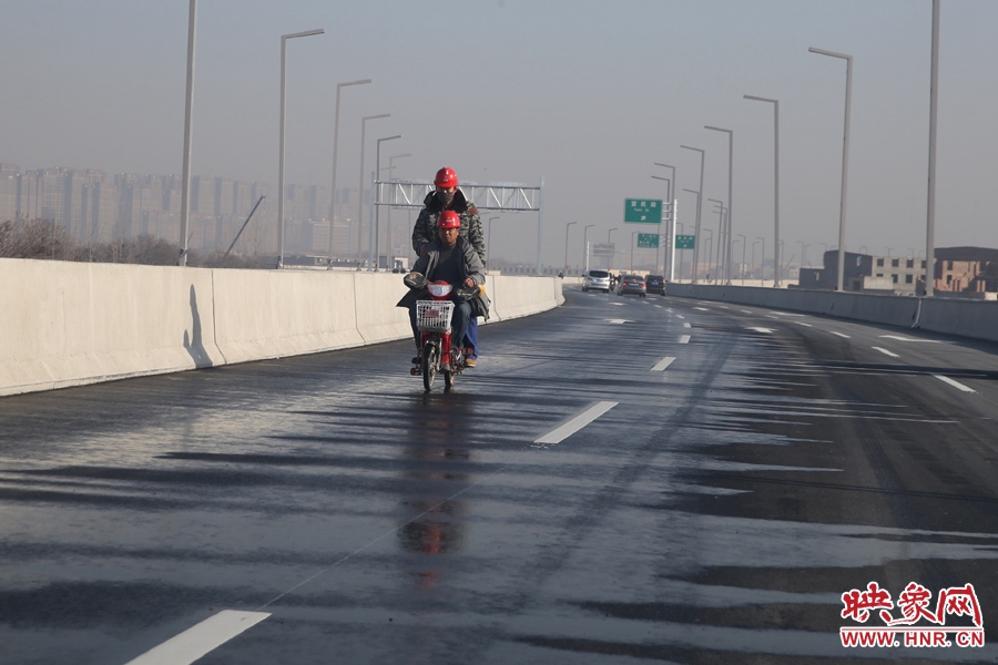 兩名工人騎車經(jīng)過灑水養(yǎng)護路面。