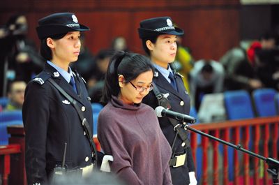 被告人盧梅低著頭，站在朝陽法院刑事審判庭的被告席上。